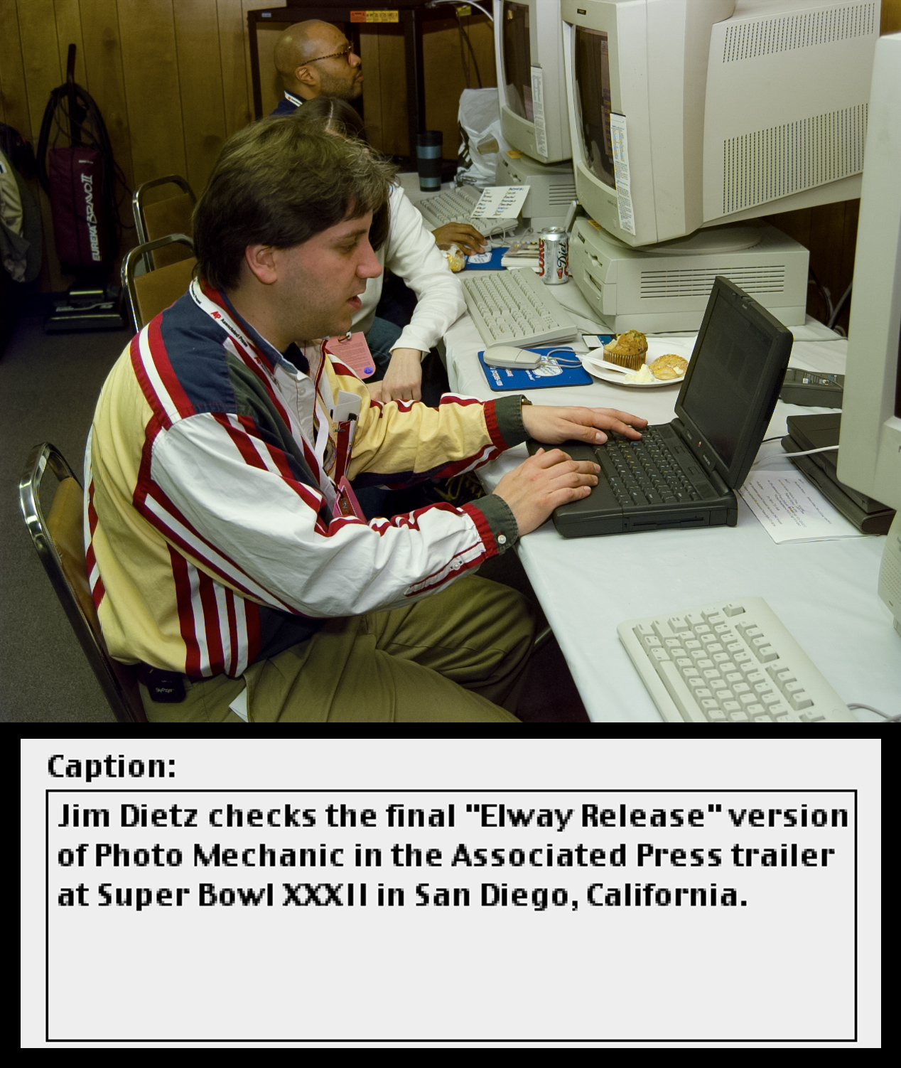 A man in a colorful shirt sits at a vintage computer laptop