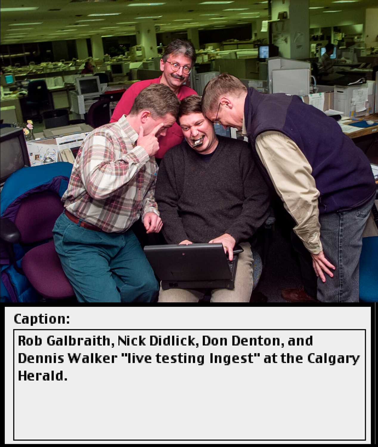 Four men gathered around a laptop computer gesturing animatedly